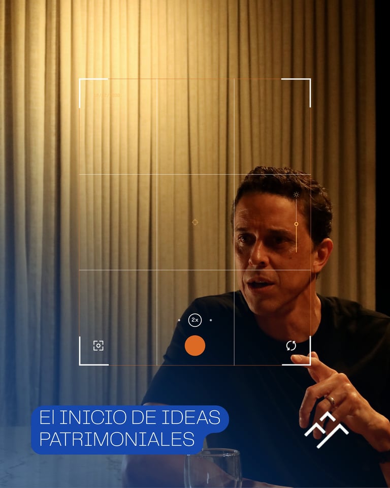 Man speaking in front of vertical striped background with blue text reading El Inicio de Ideas Patrimoniales